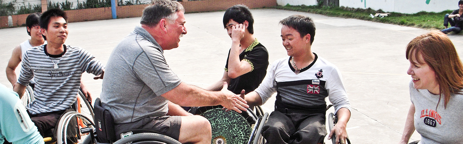 American man seated in a wheelchair extends his hand to two Chinese delegates.