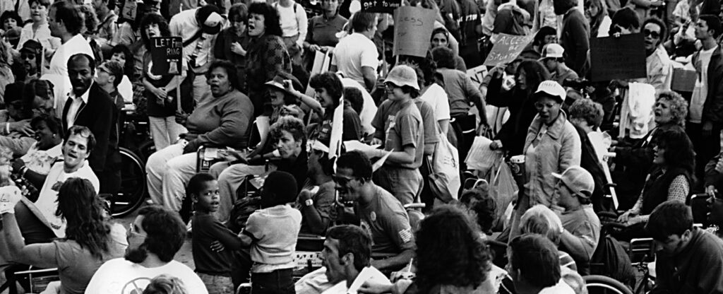 black and white photo of dozens of people gathered - including people of color and people with visible disabilities - in protest