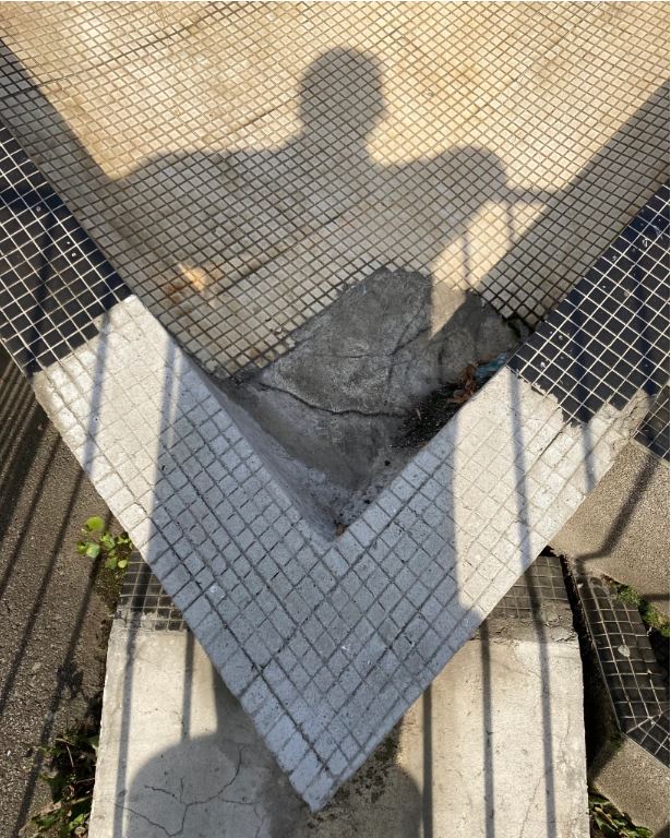 A shadow - presumably Stephen's - is cast on a black and white tile mosaic pool or planter. The shadow is a figure resting arms on a railing.
