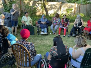 WILD women seated in a circle in a grass backyard setting. One delegate speaks while holding a candle.