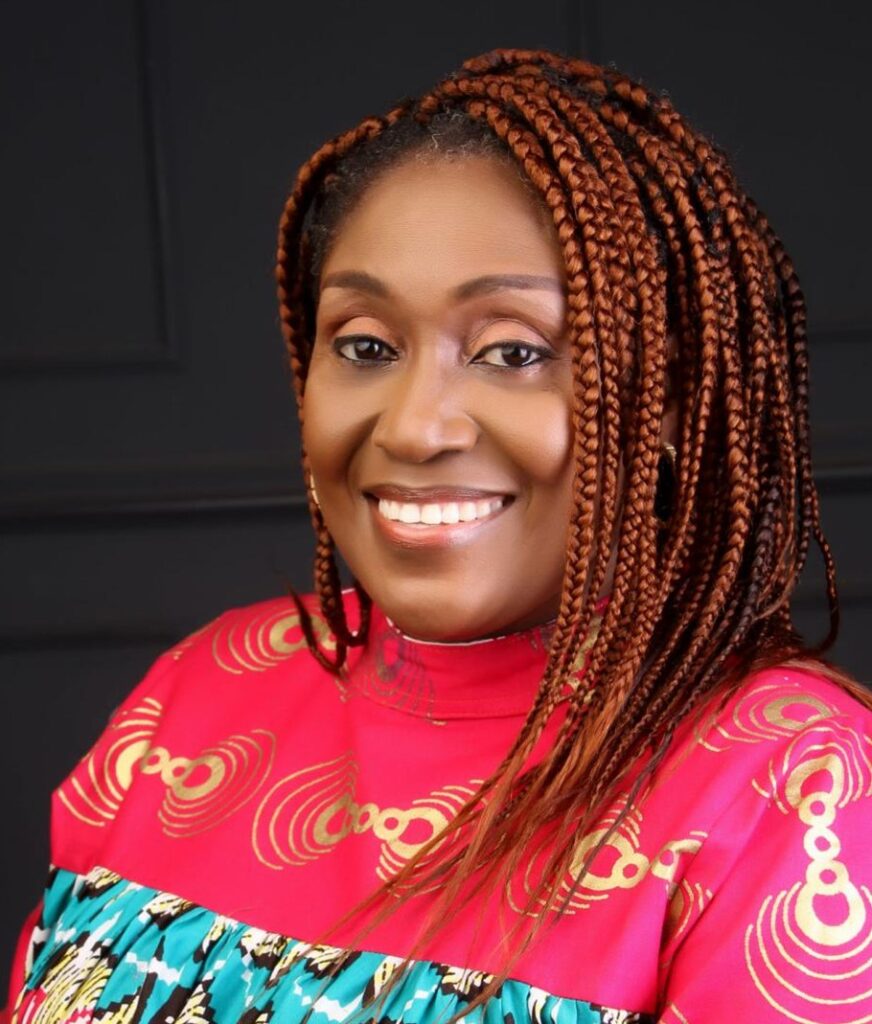 Ekaete portrait, smiling brightly at camera wearing braids and brightly color and pattern shirt