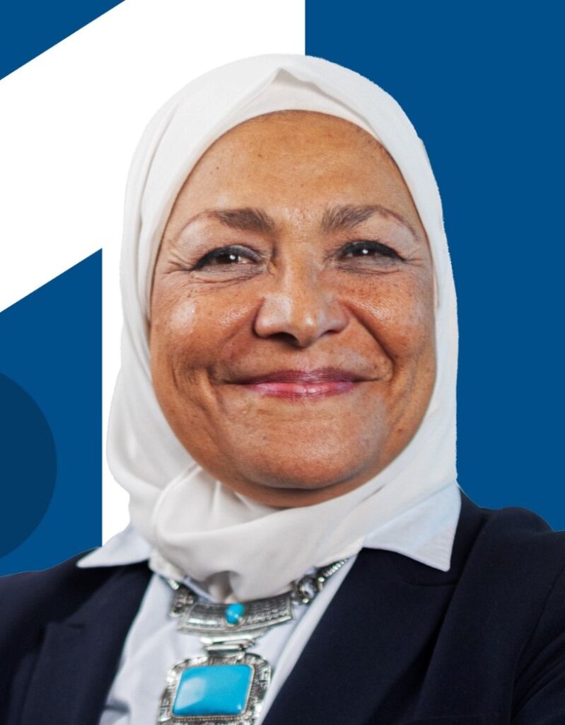 Portrait of Hanan smiling in direction of camera wearing white scarf around her face and turquoise necklace