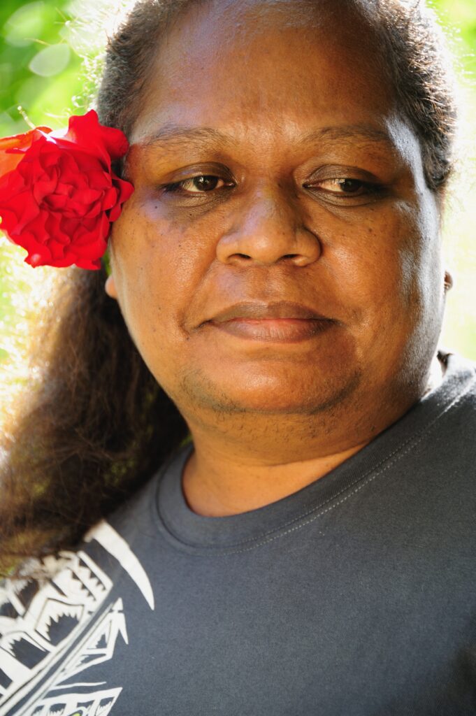 Lanieta wears serene expression on her face and wears red flower behind her ear as she gazes away from the camera