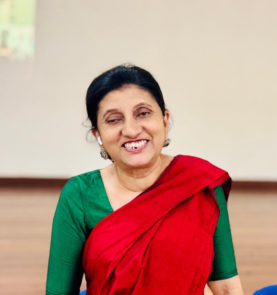 Manique smiles brightly, eyes averted and wearing bright red and green sari